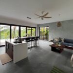 Modern open-plan living room, dining area, and kitchen in a contemporary Kerala home with abundant natural light.