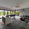 Modern open-plan living room, dining area, and kitchen in a contemporary Kerala home with abundant natural light.